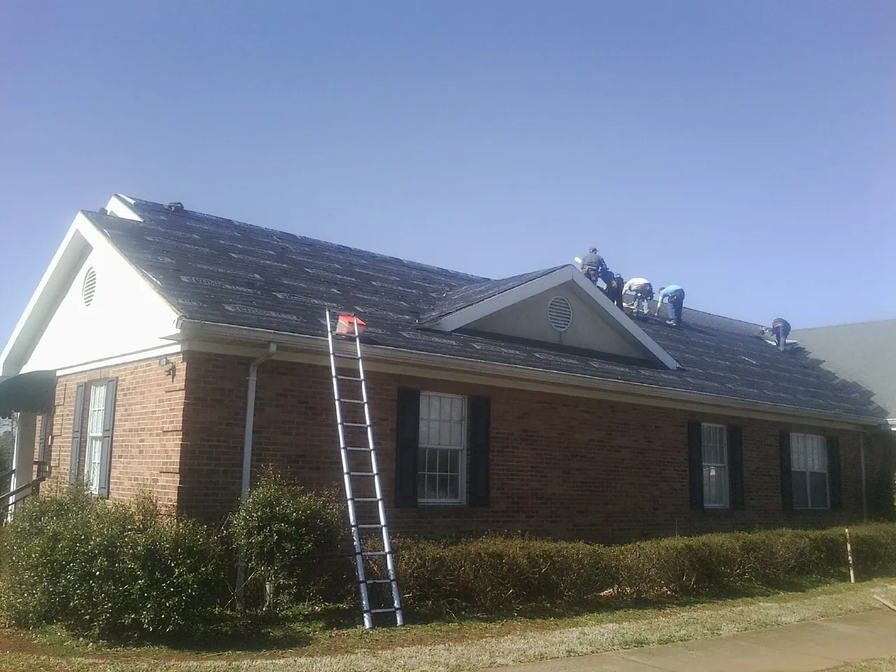 Crew tearing shingles off a brick ranch roof with a ladder set — Metal Roof Repair work by our crew in Greenwich